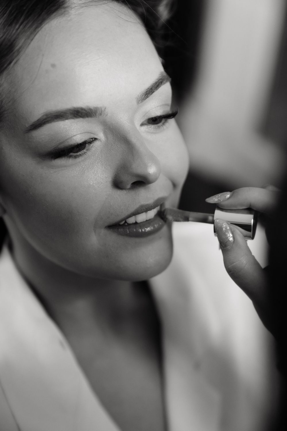 Black and white photo of a bride having lipstick applied by a makeup artist during bridal preparations.