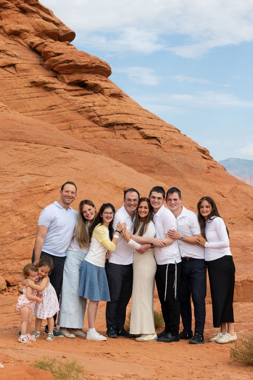 Family group photo posing together in front of red rock formations in a desert landscape under a partly cloudy sky.