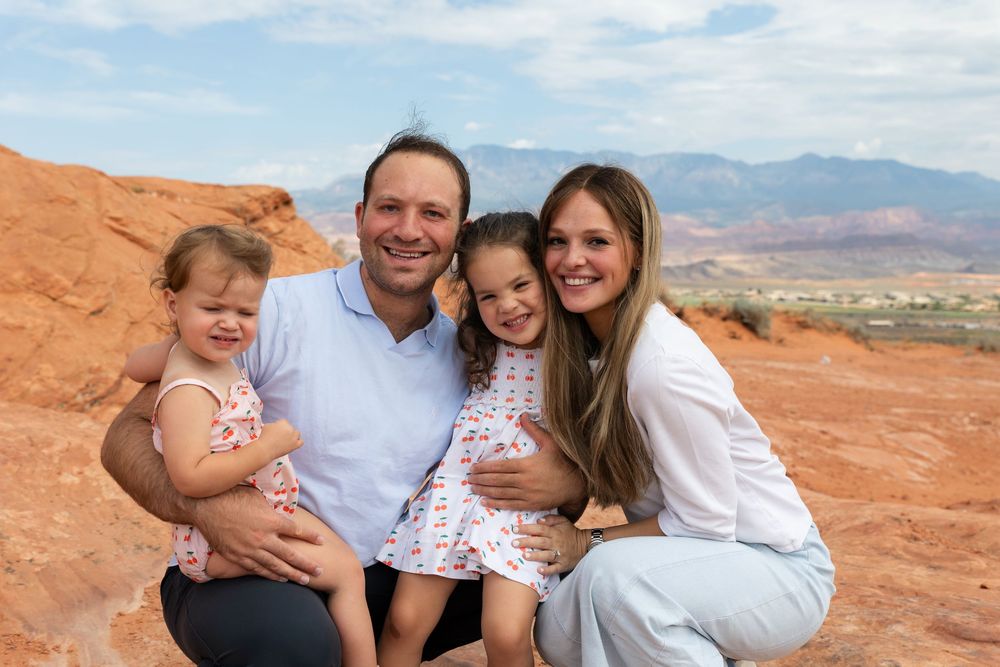 Family of four smiling together on red rock desert landscape with mountain views in the background.
