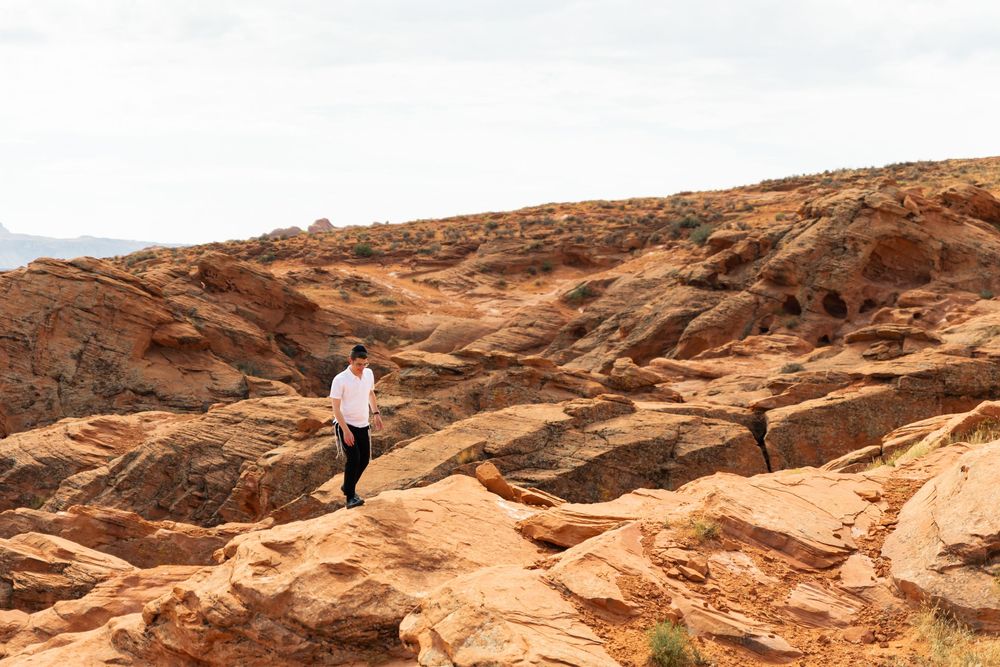 A person hiking on red rock formations in a desert landscape under an overcast sky.