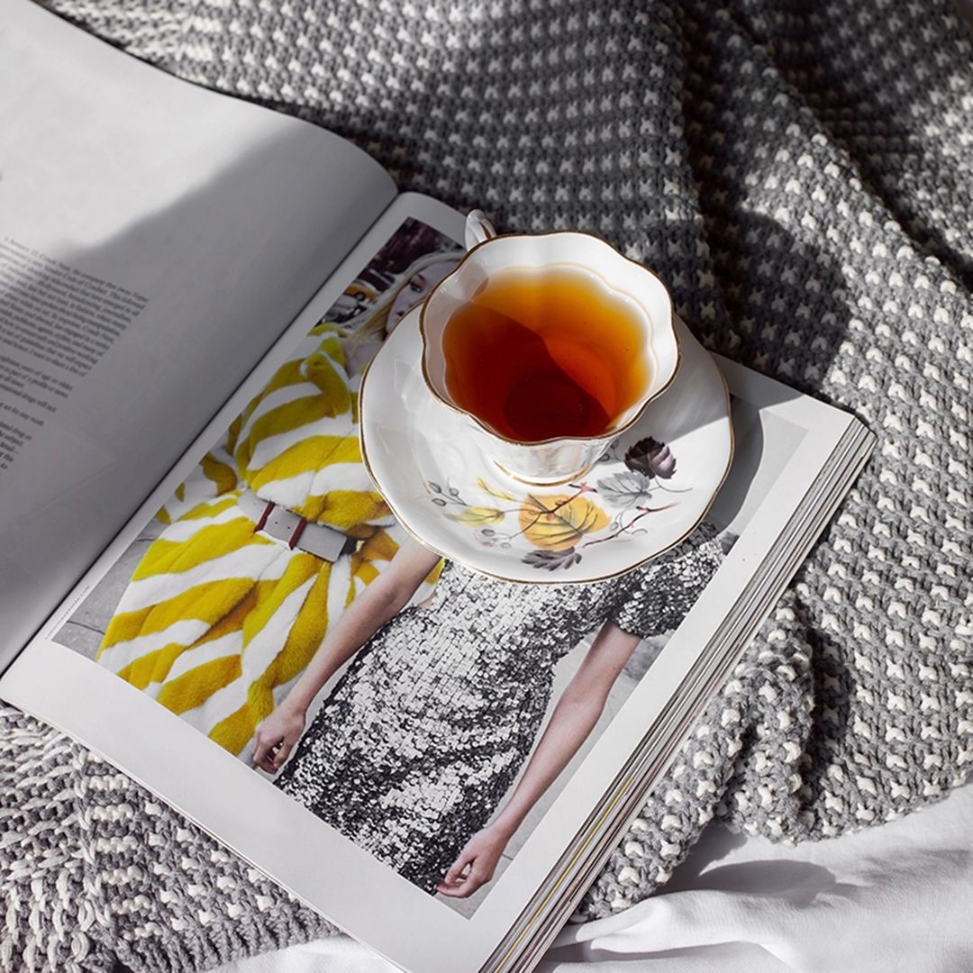 Cup of English breakfast tea on open magazine with gray knit blanket.