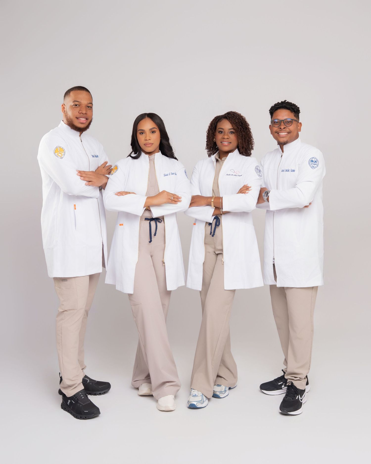 Four medical professionals in white lab coats pose confidently with arms crossed against a light gray background.