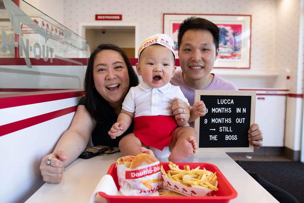 Family celebrating baby Lucca's 9-month milestone at In-N-Out Burger, holding a sign reading Still the Boss.
