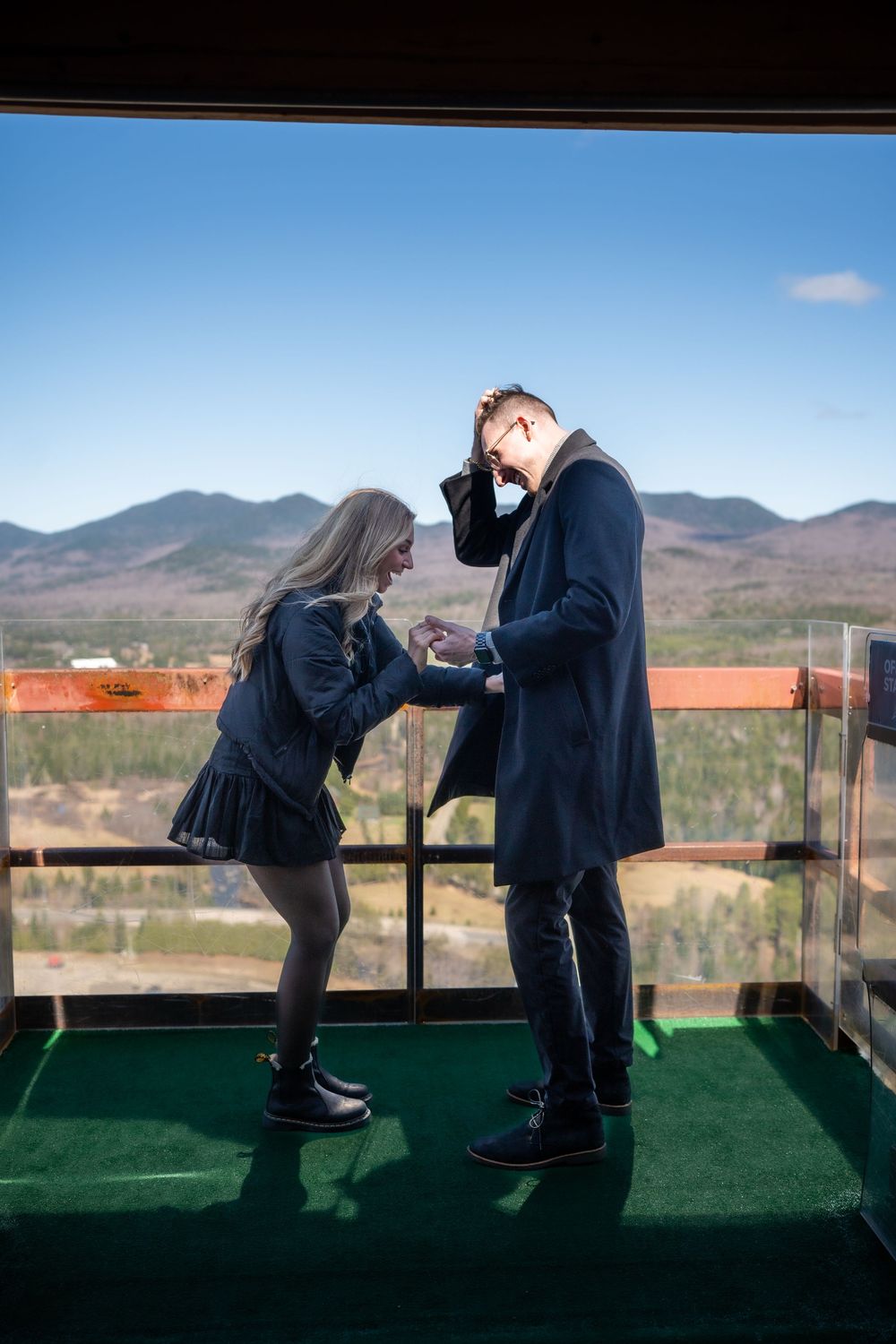 Couple sharing a romantic moment on a scenic overlook with mountain views and blue sky backdrop.