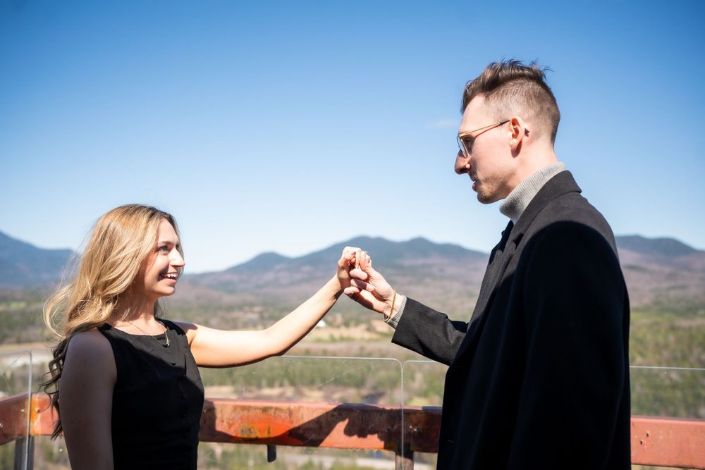 Couple in black attire holding hands on a scenic mountain overlook under a clear blue sky.