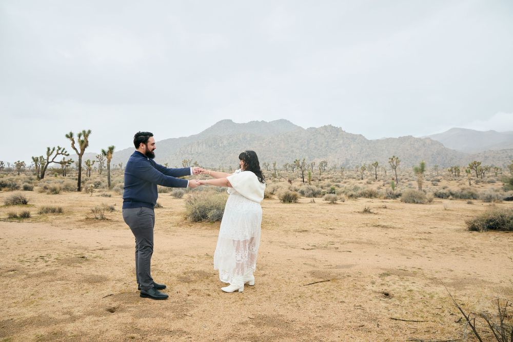 Couple dancing together in Joshua Tree desert landscape with mountains in background.