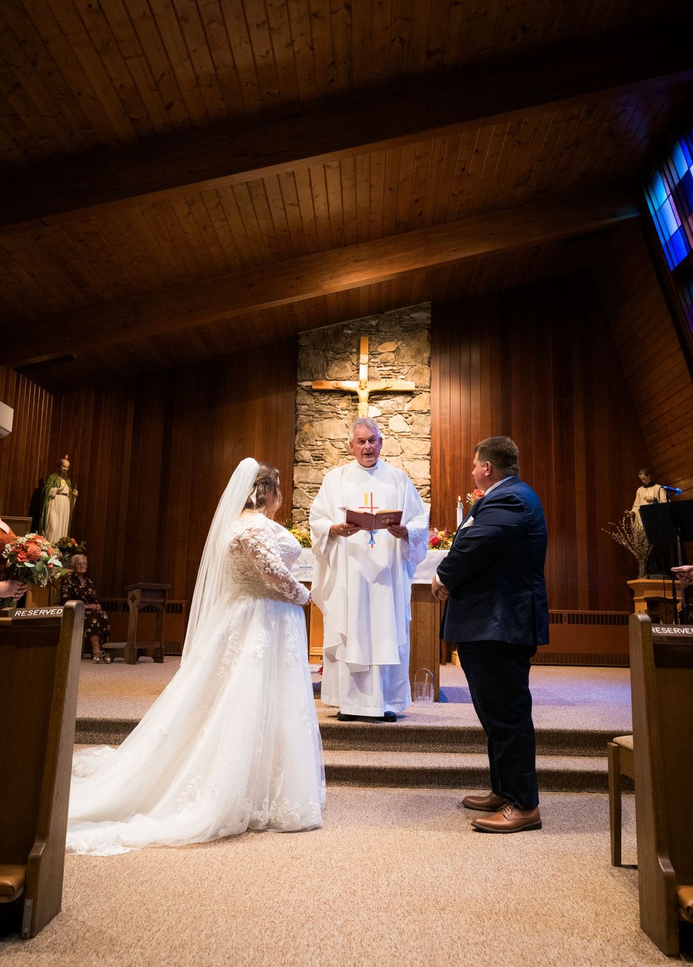 Bride and groom exchange vows before priest at Catholic church altar.