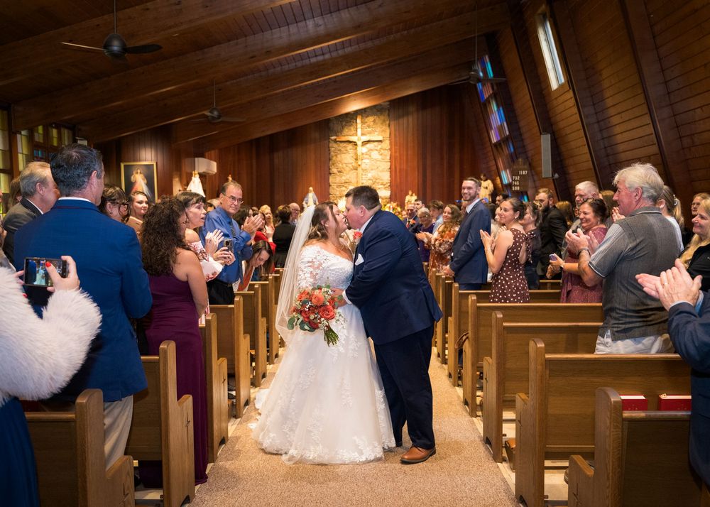 Newlyweds share a first kiss at the altar as guests applaud in a wood-paneled church wedding ceremony.
