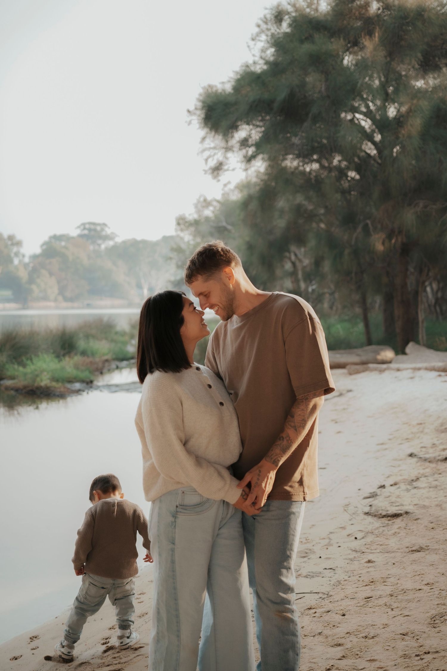 Couple sharing a romantic moment on a sandy beach at golden hour, woman in white dress, man in white shirt.