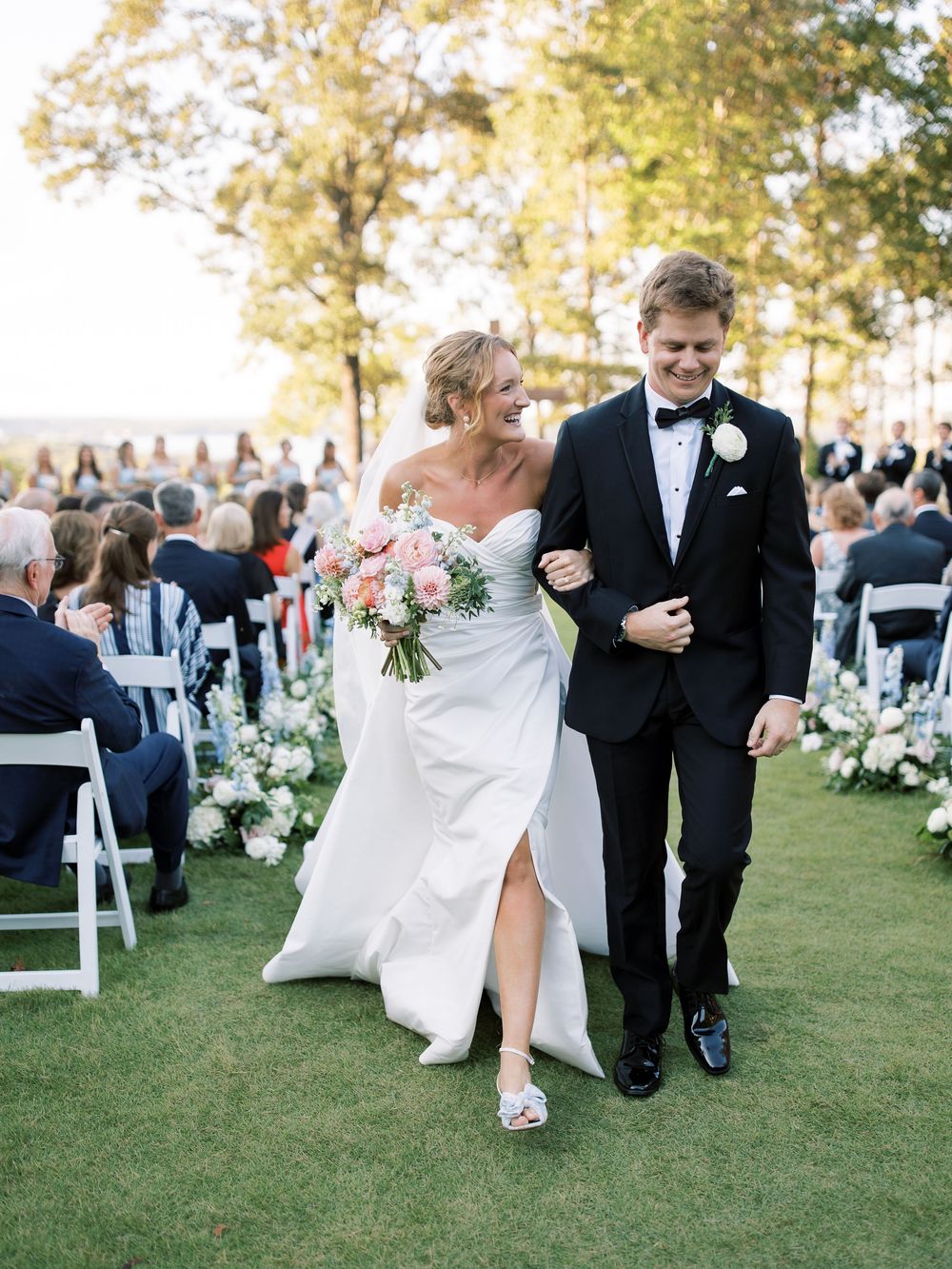 Outdoor wedding ceremony setup with white chairs and floral arrangements on a grassy lawn.