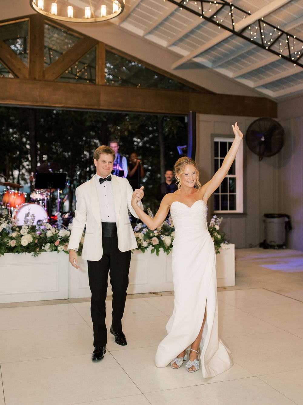 Wedding reception dance floor under wooden beamed ceiling with string lights.
