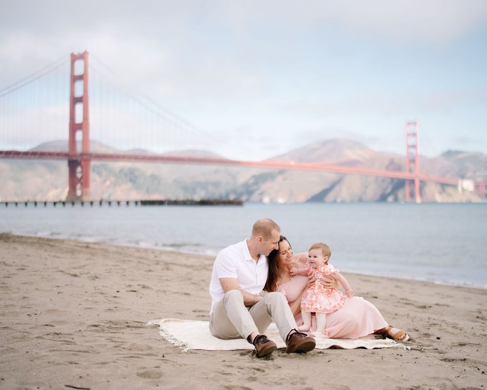 Family sitting on a blanket at Baker Beach with the Golden Gate Bridge in the background in San Francisco.