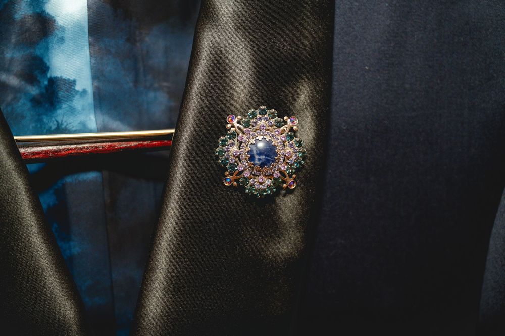 Elegant ornate brooch with blue gemstone center and intricate floral metalwork pinned on black satin fabric.