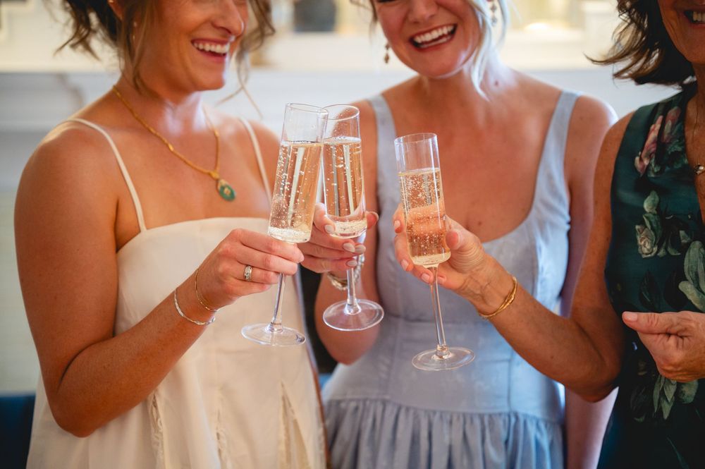Three women smiling and toasting with champagne flutes at a celebration, wearing elegant dresses.