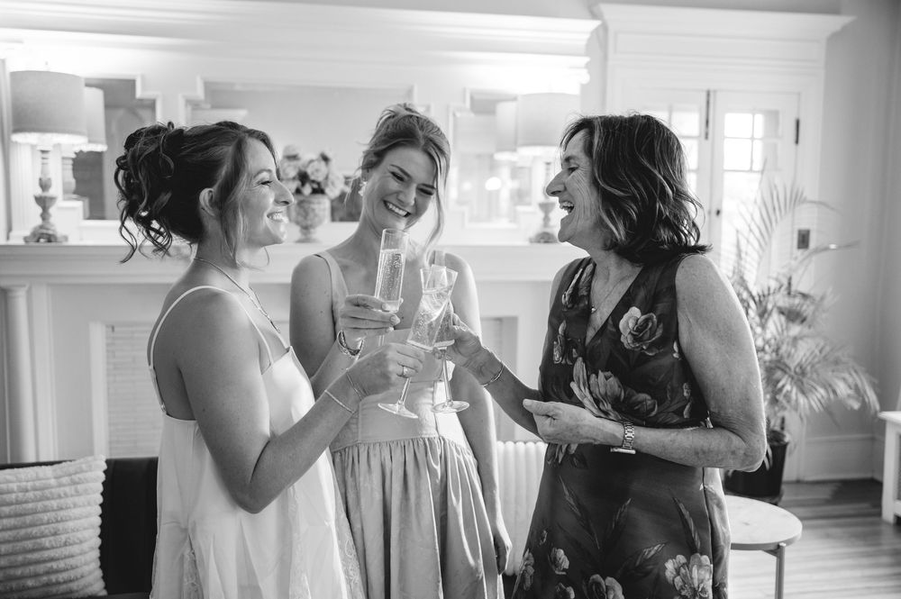 Three women laughing and toasting with champagne glasses in a bright room during a wedding celebration.
