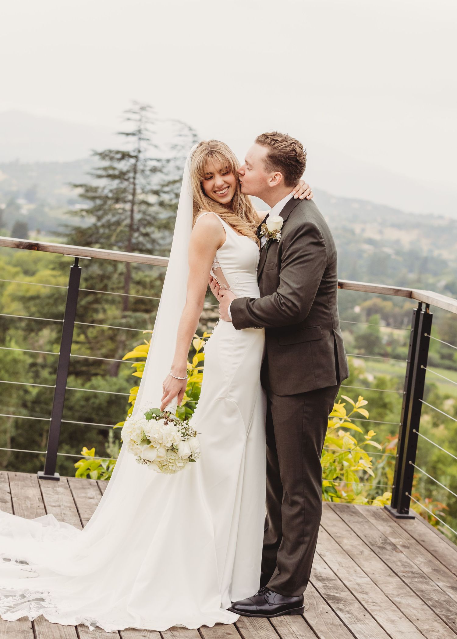 Bride and groom sharing a kiss between ornate wrought iron gates, bride holding white bouquet in elegant wedding attire.