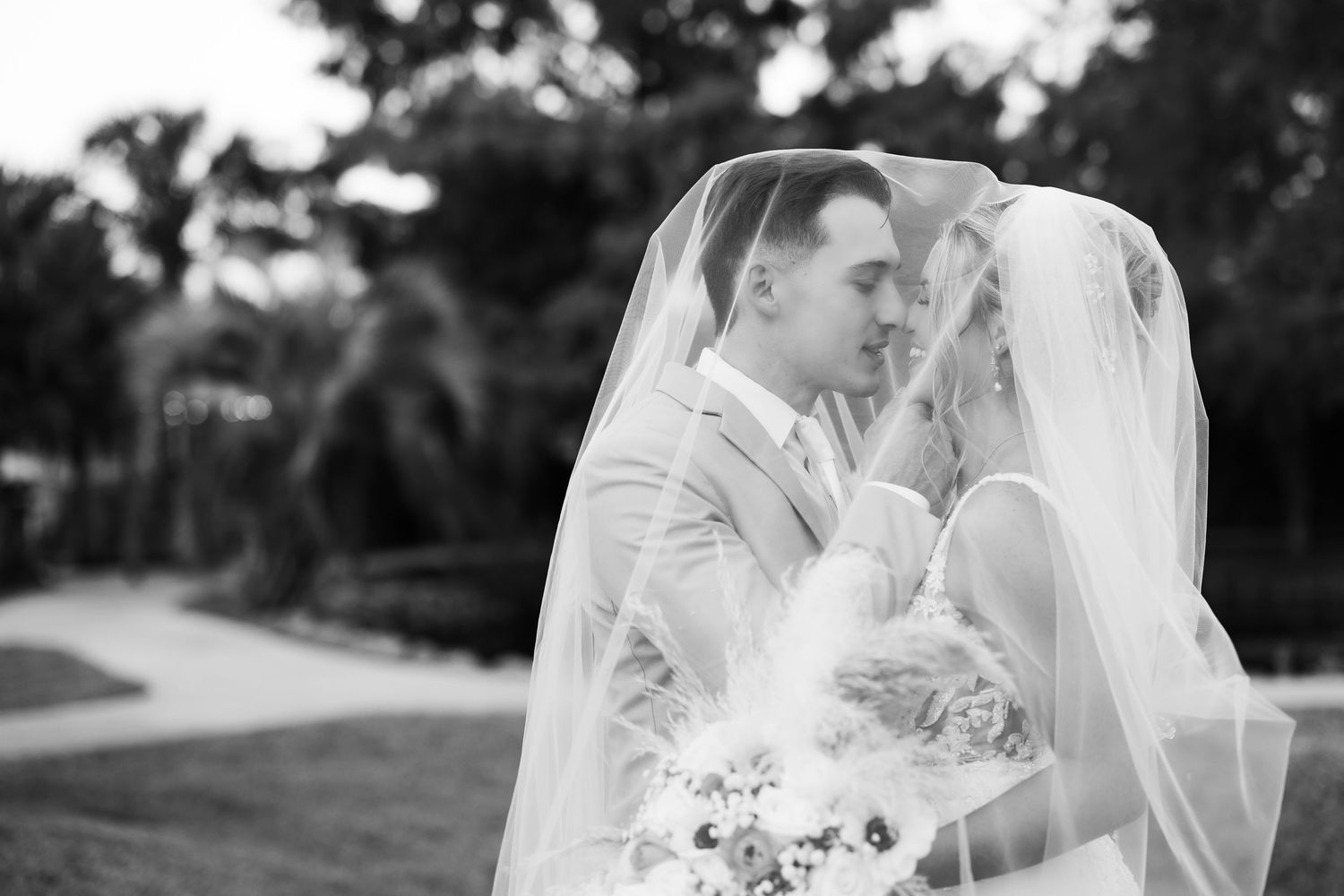 Bride and groom walk down outdoor wedding aisle holding hands, bride in white gown with bouquet, groom in black tuxedo.