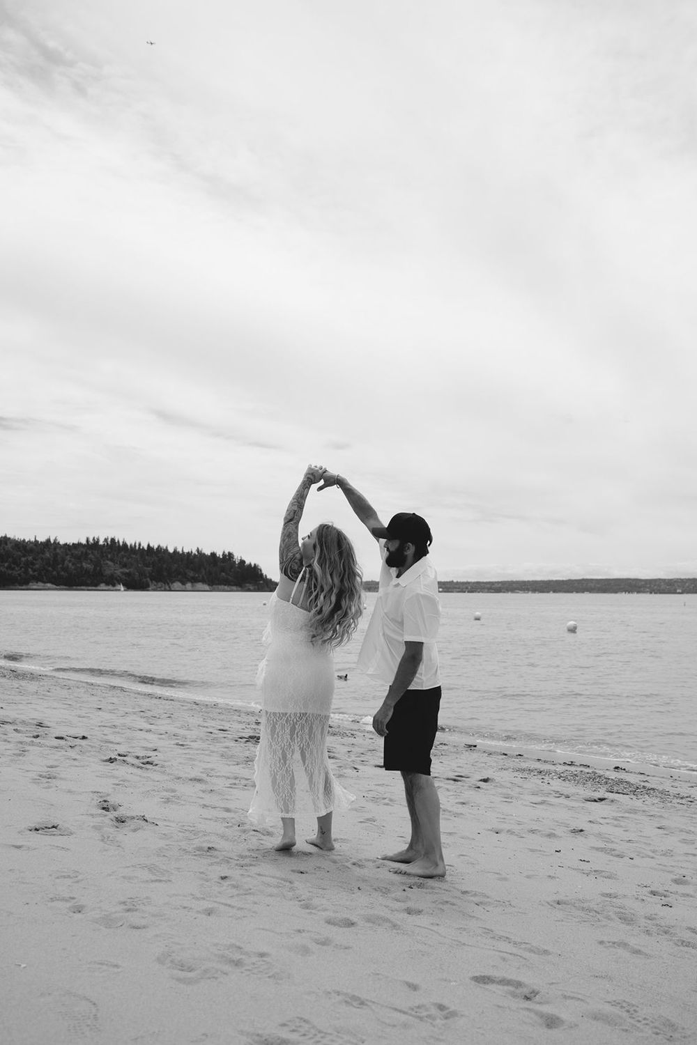Couple dancing on beach, man spinning woman, black and white romantic photo.