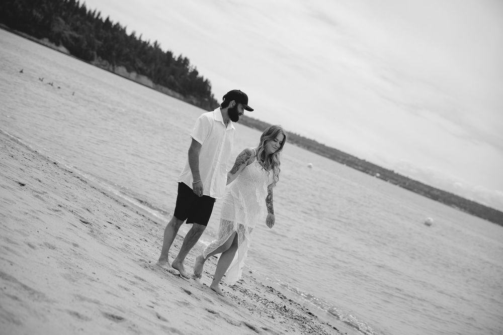 Couple walking hand in hand on a sandy beach in black and white photo.