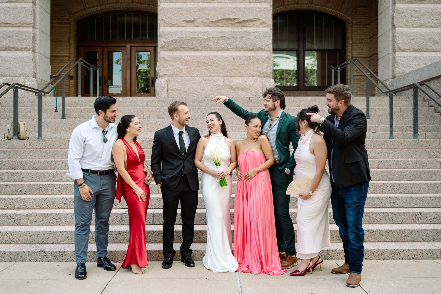 Bride, groom and friends sharing a laugh on the steps of a Houston courthouse.