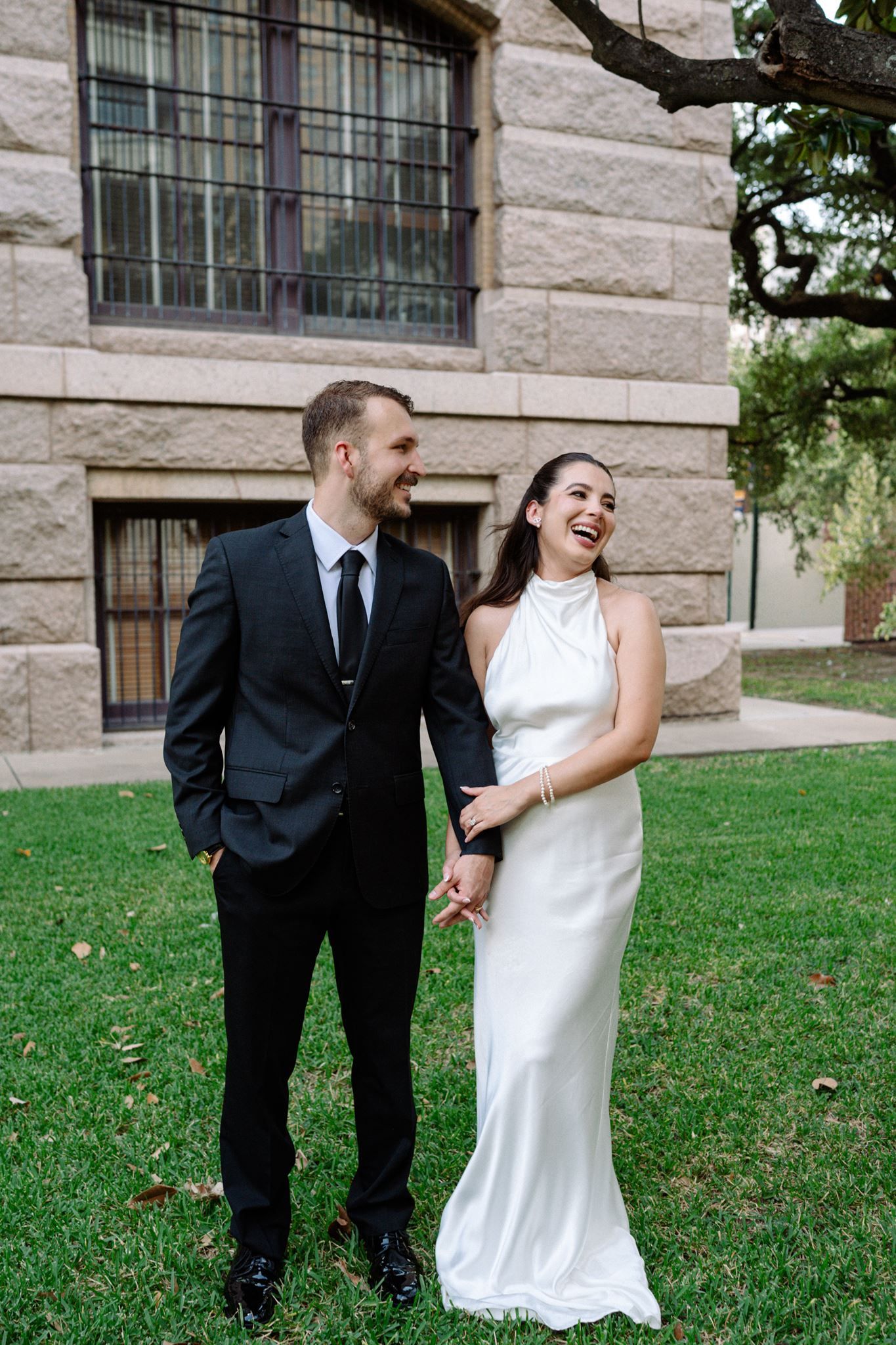 Bride and groom sharing a hearty laugh on the lawn of the historic 1910 Courthouse.
