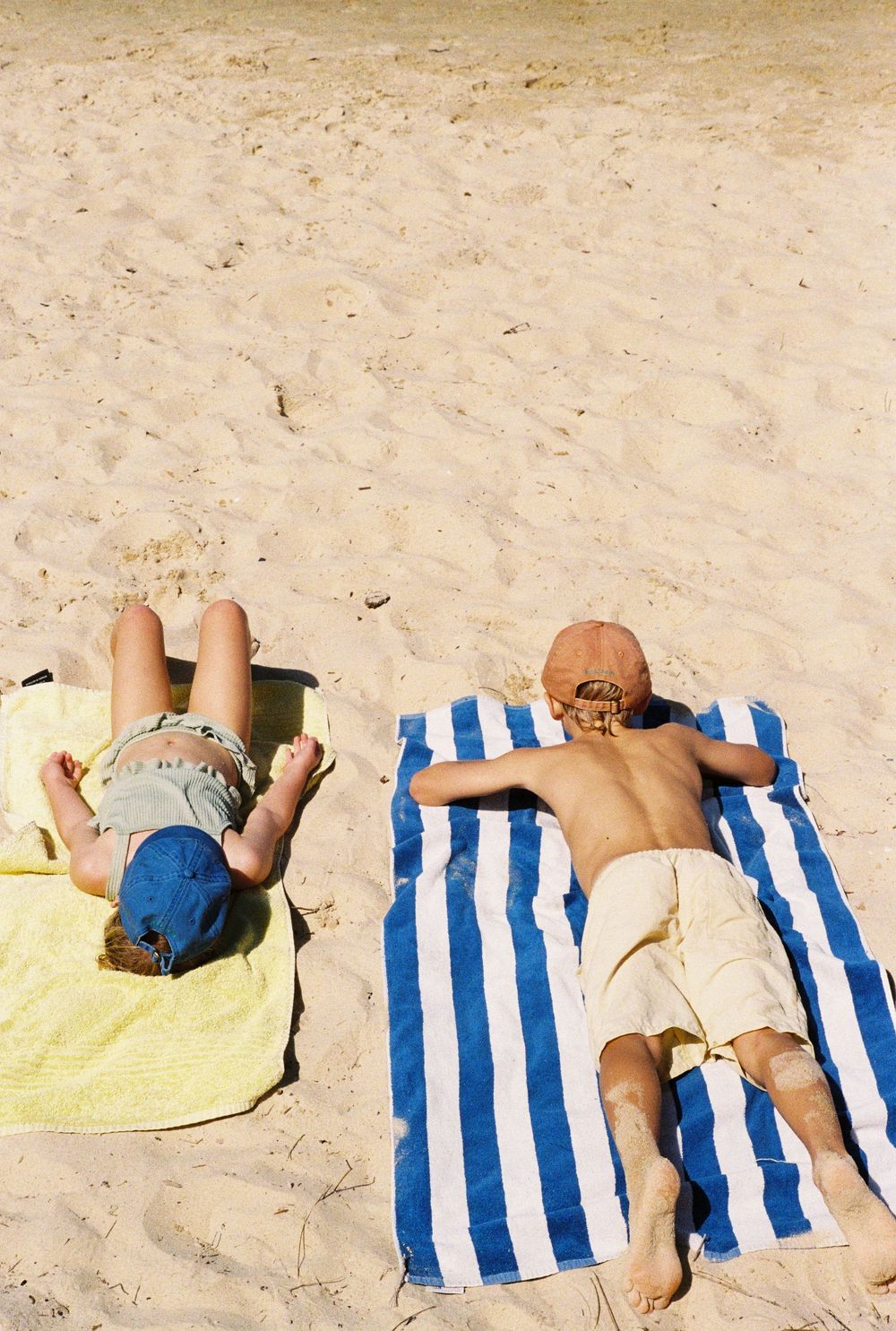 Two people sunbathing on colorful towels on a sandy beach on a sunny day.