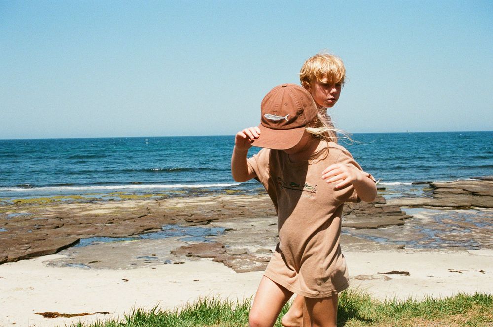 Two children playing at a rocky beach, one giving the other a piggyback ride on a sunny day.