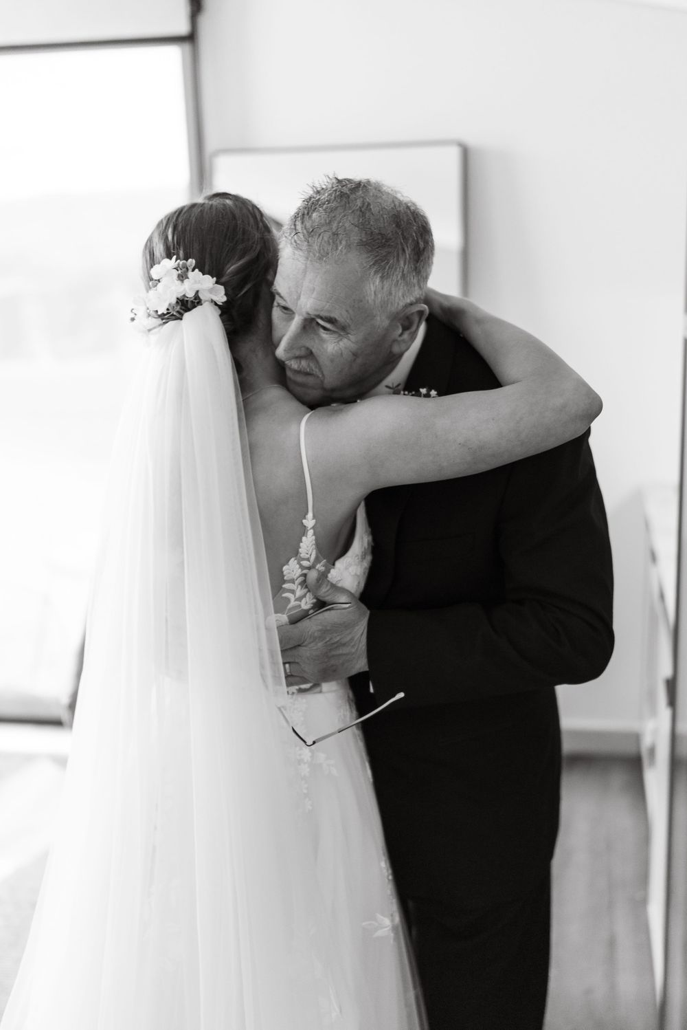 Black and white photo of a bride and older man sharing an emotional hug on her wedding day.