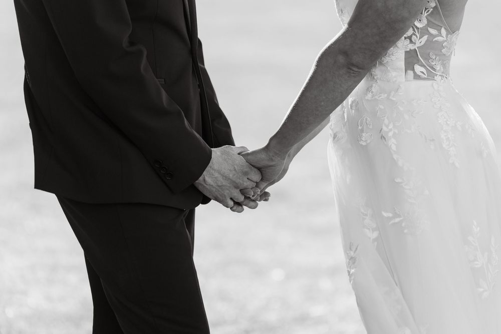 Black and white photo of bride and groom holding hands at wedding ceremony.