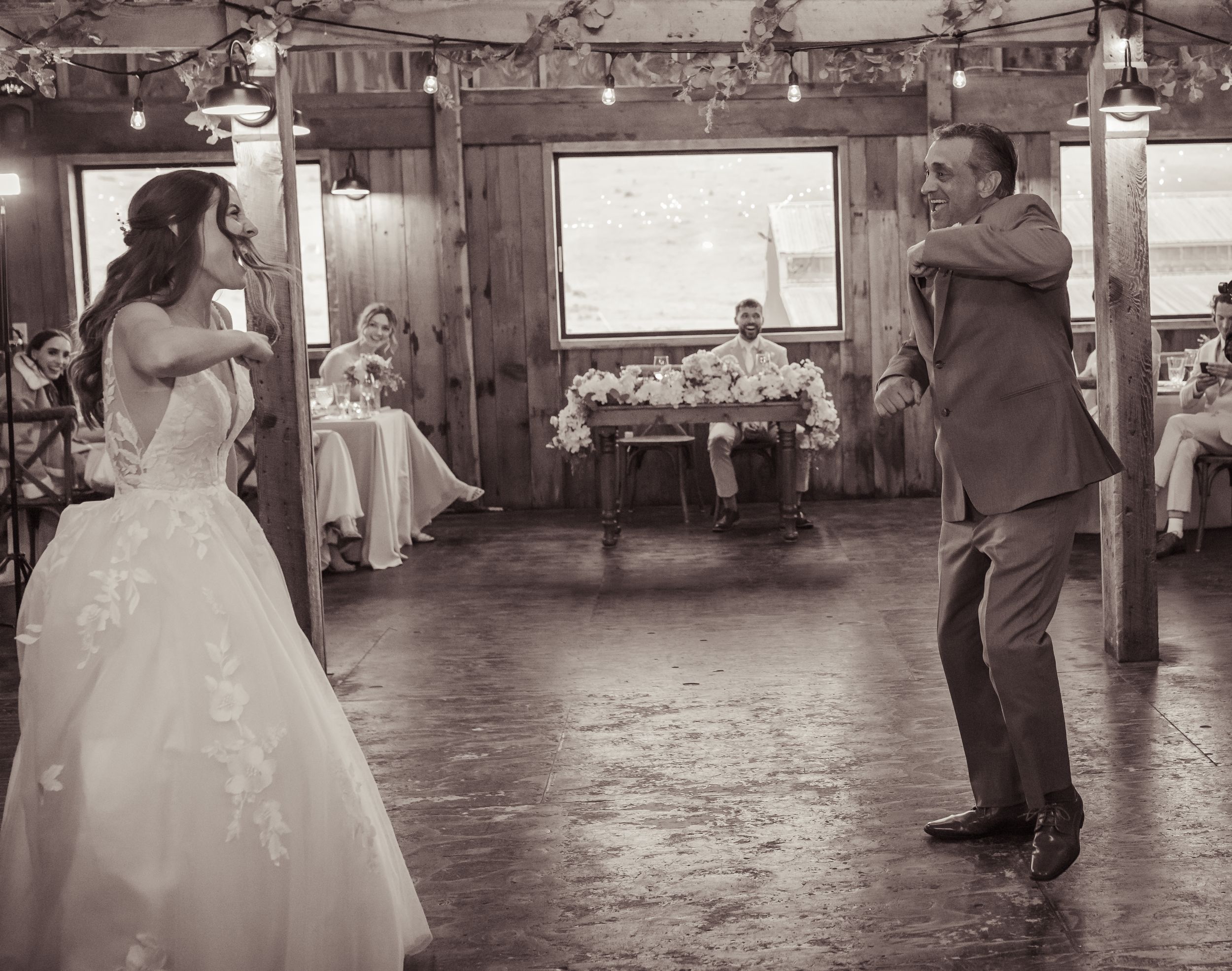 Black and white photo of bride and groom sharing first dance at rustic barn wedding reception.