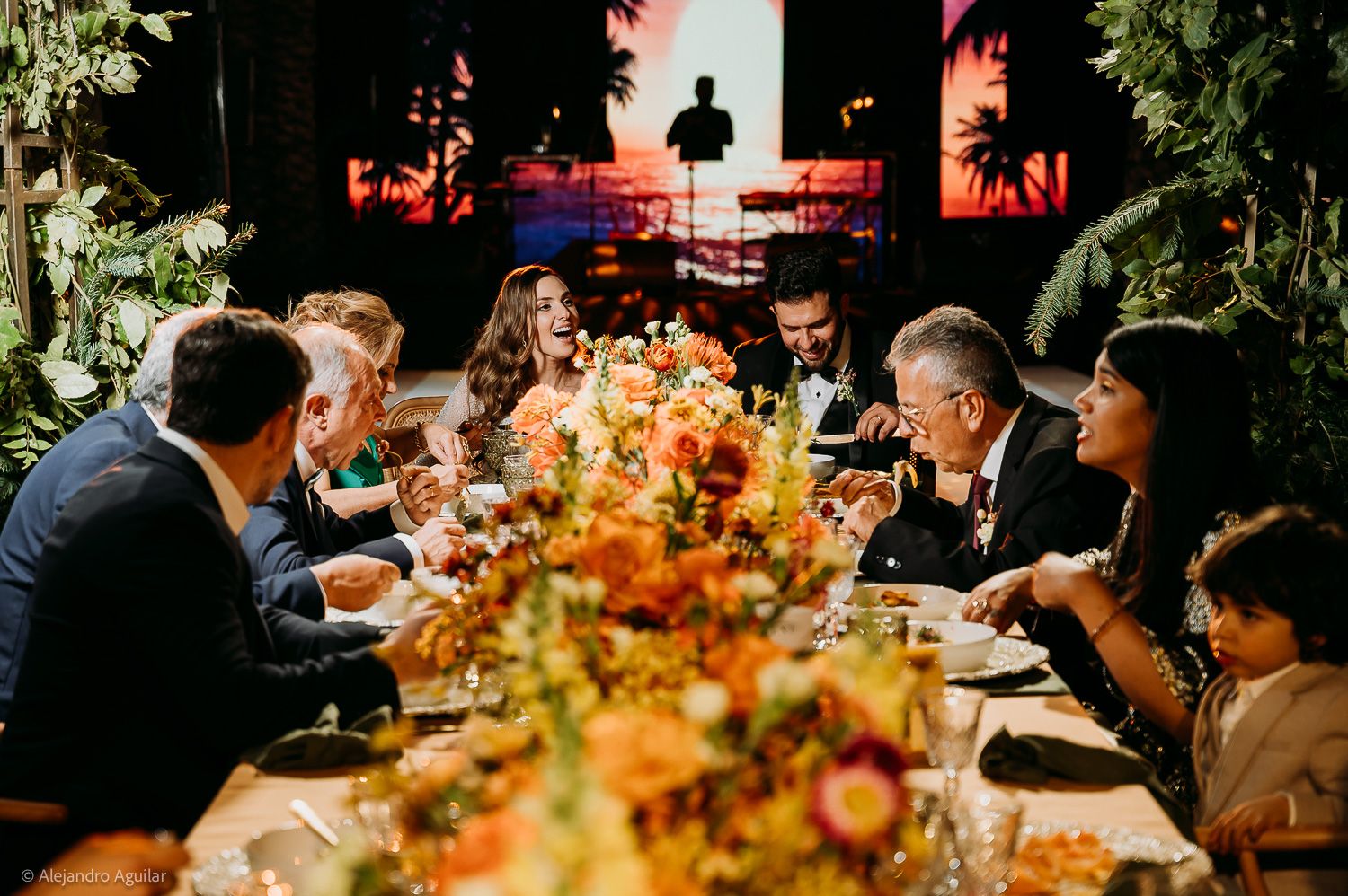 Guests gathered around a festive dinner table adorned with vibrant orange floral arrangements at an elegant evening event.