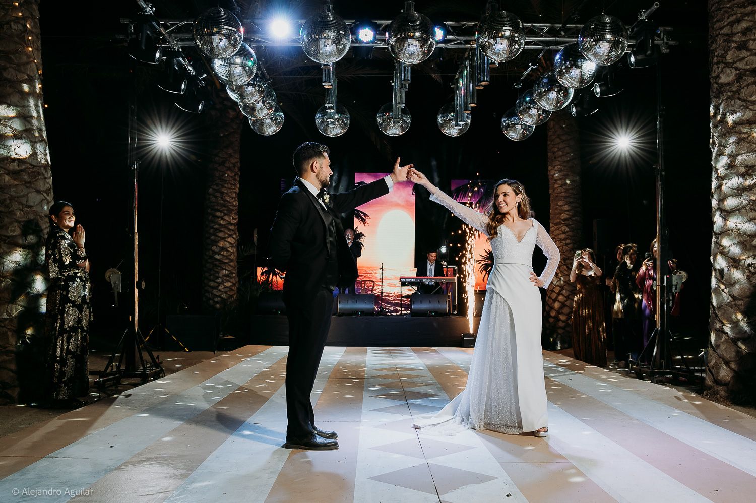 Bride and groom share first dance on illuminated dance floor with disco balls and sparkling lights at elegant wedding reception.