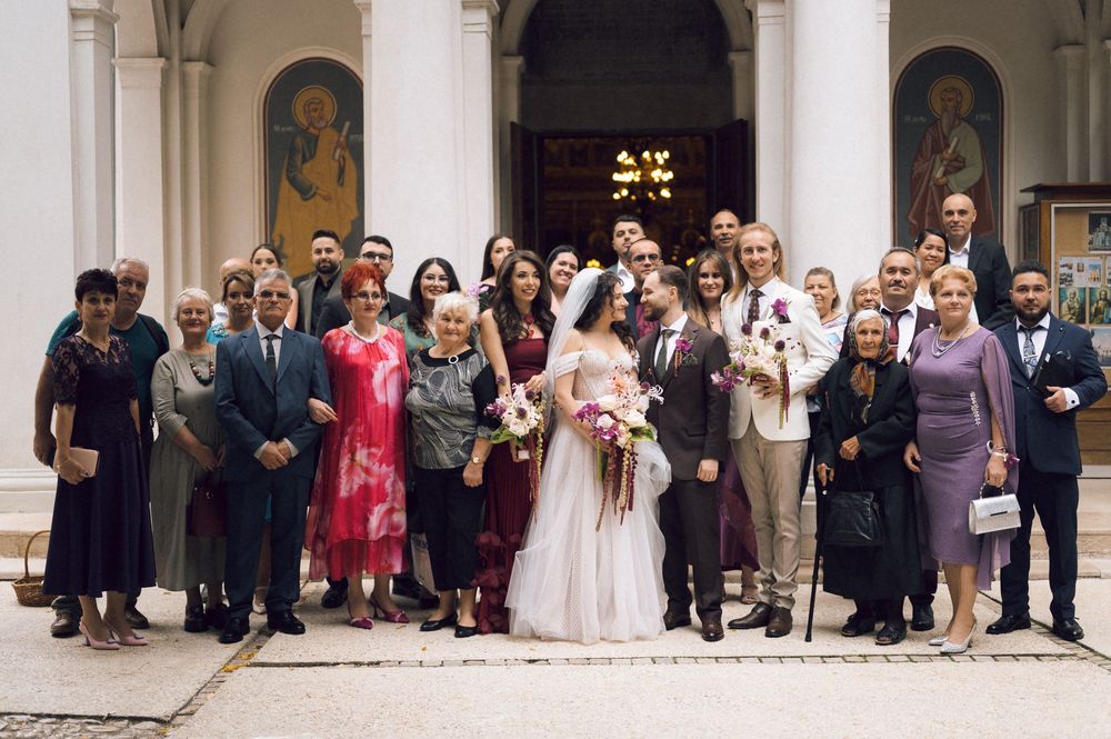 Wedding group photo with bride and groom surrounded by family and friends outside a historic church.