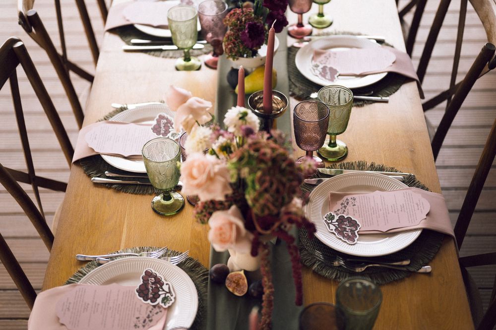 Elegant wedding table setting with blush florals, green goblets, and a sage runner on a wooden table.