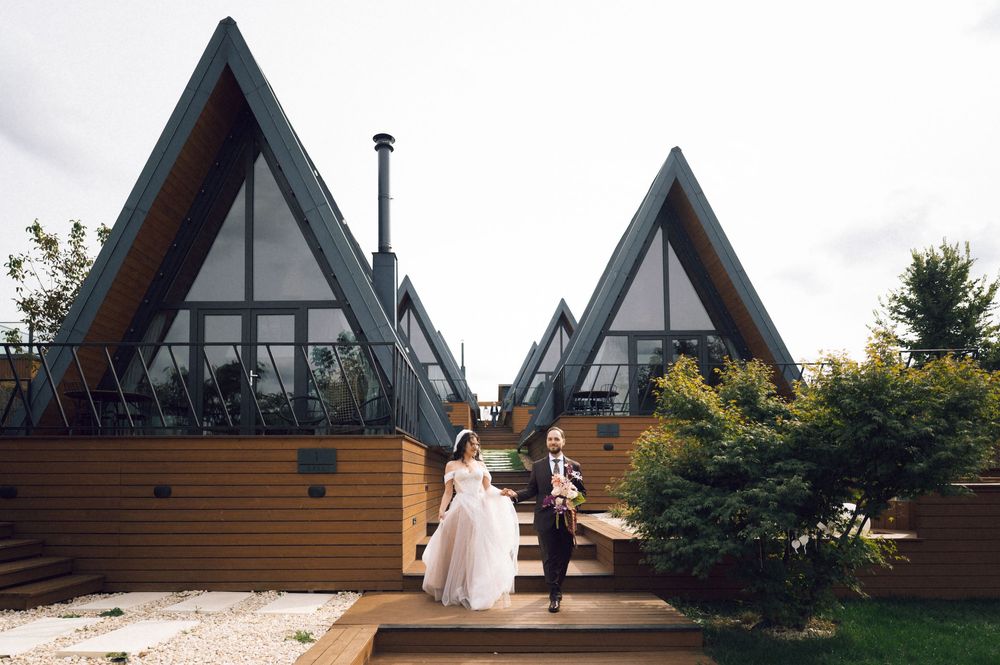 Bride and groom walk hand in hand outside unique A-frame wedding venue with dramatic triangular architecture.