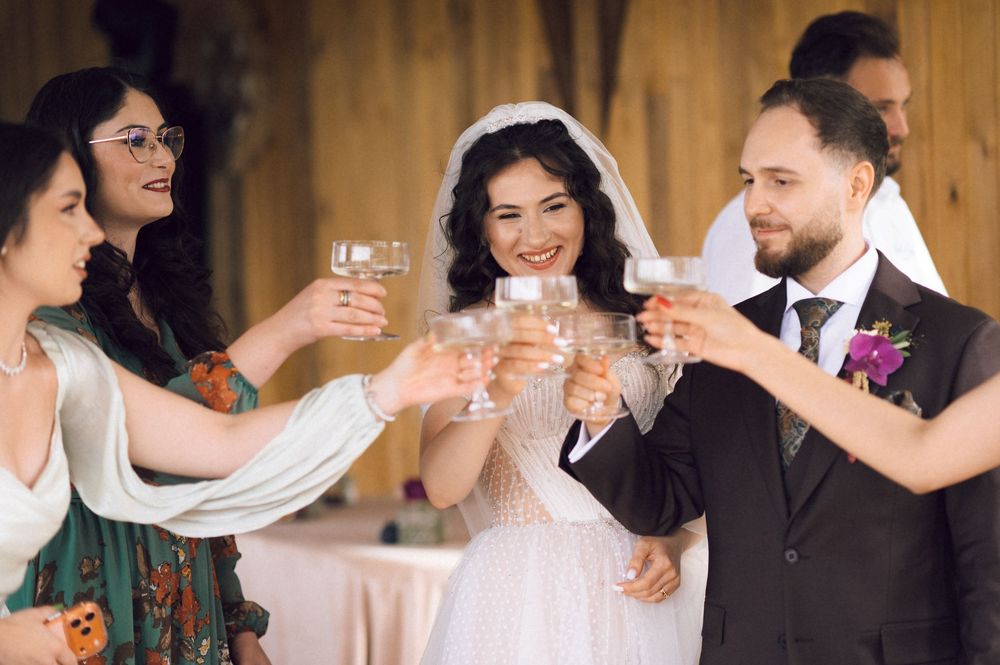 Bride and groom toasting with guests at wedding reception, smiling and clinking champagne glasses.