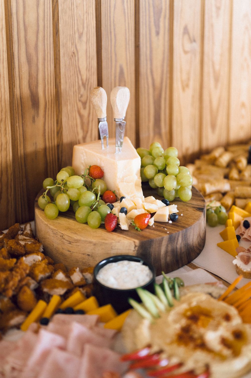 Elegant charcuterie board with parmesan cheese, green grapes, strawberries, and cheese knives on a rustic wooden platter.