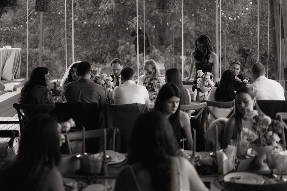 Black and white photo of elegantly dressed guests dining at a sophisticated indoor wedding reception event.