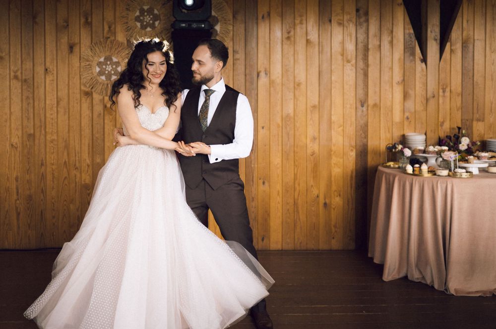 Bride and groom share their first dance in a rustic wooden venue, bride wearing a flowing white gown.