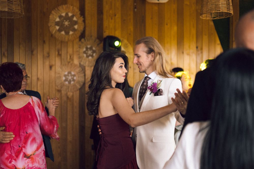 Couple dancing at a wedding reception, man in white suit with boutonniere, woman in burgundy dress.