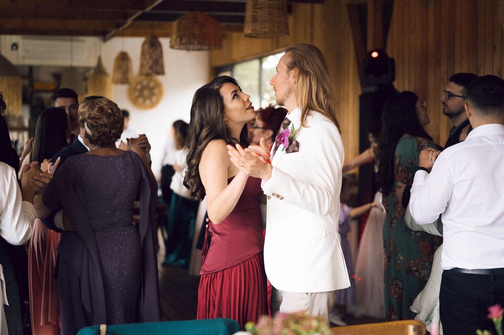 Couple sharing a romantic dance at a wedding reception in a warmly lit venue with guests in formal attire.