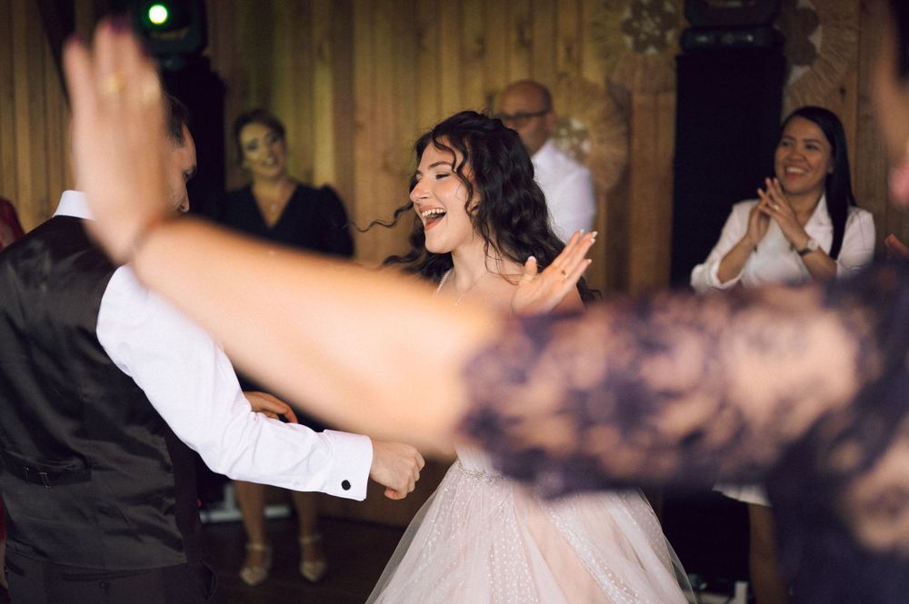 Bride and groom share joyful first dance at wedding reception with guests clapping in background.