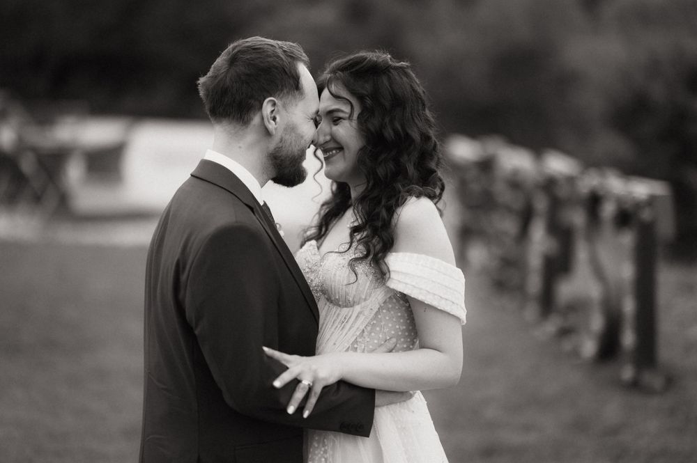 Black and white photo of a couple in wedding attire sharing an intimate moment outdoors near a rustic fence.