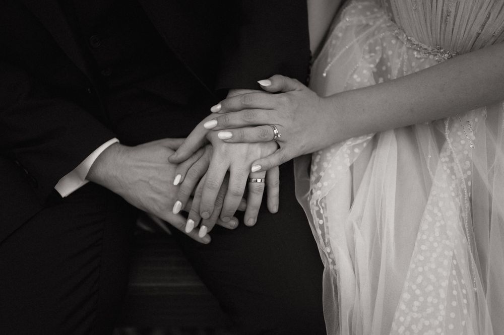 Black and white photo of bride and groom holding hands, showing wedding rings during ceremony.