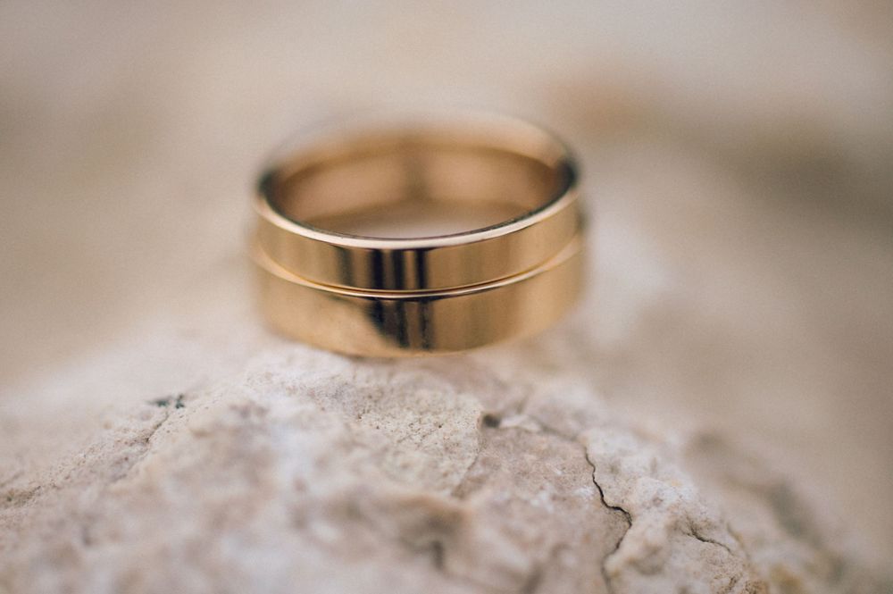 Gold wedding band ring resting on a textured stone surface, with a polished finish and elegant grooved design.