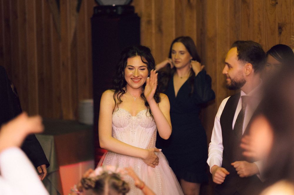 Young woman in pink dress smiling at indoor party celebration with guests in background.