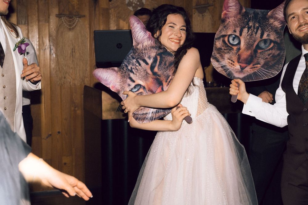 Bride in white tulle gown hugging a large cat face prop at a wedding reception dance floor.