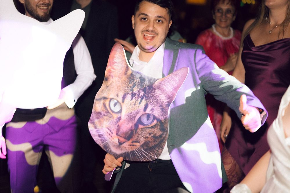 Man wearing a purple blazer with a large cat face print dancing at a festive party event.