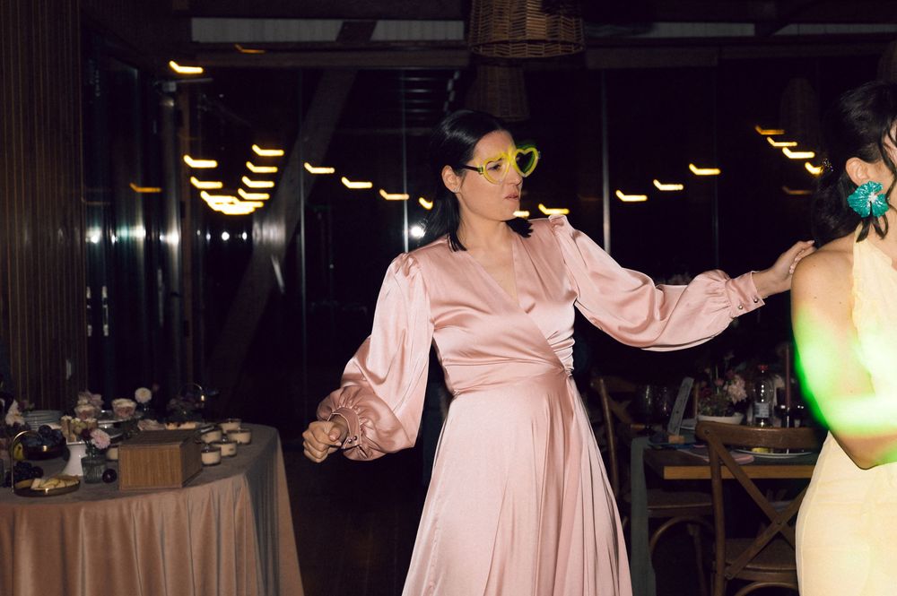 Woman in pink satin dress with yellow sunglasses dancing at an elegant indoor event.
