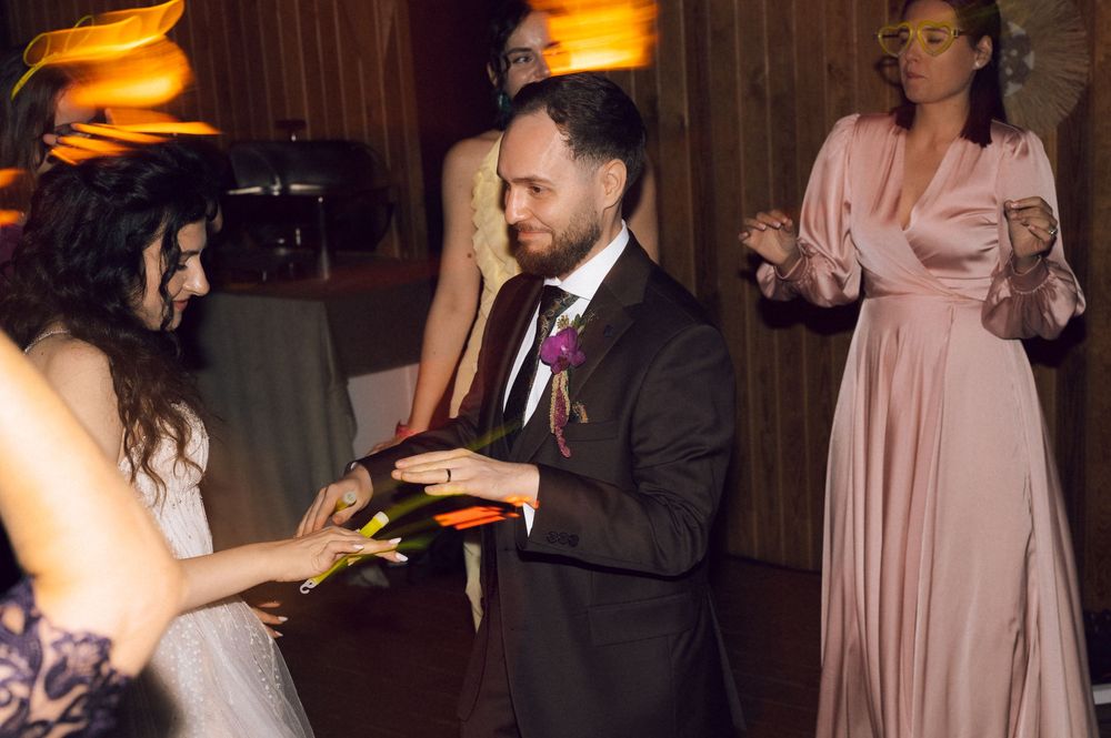 Groom in dark suit exchanges rings with bride at elegant wedding reception with bridesmaid in pink dress.